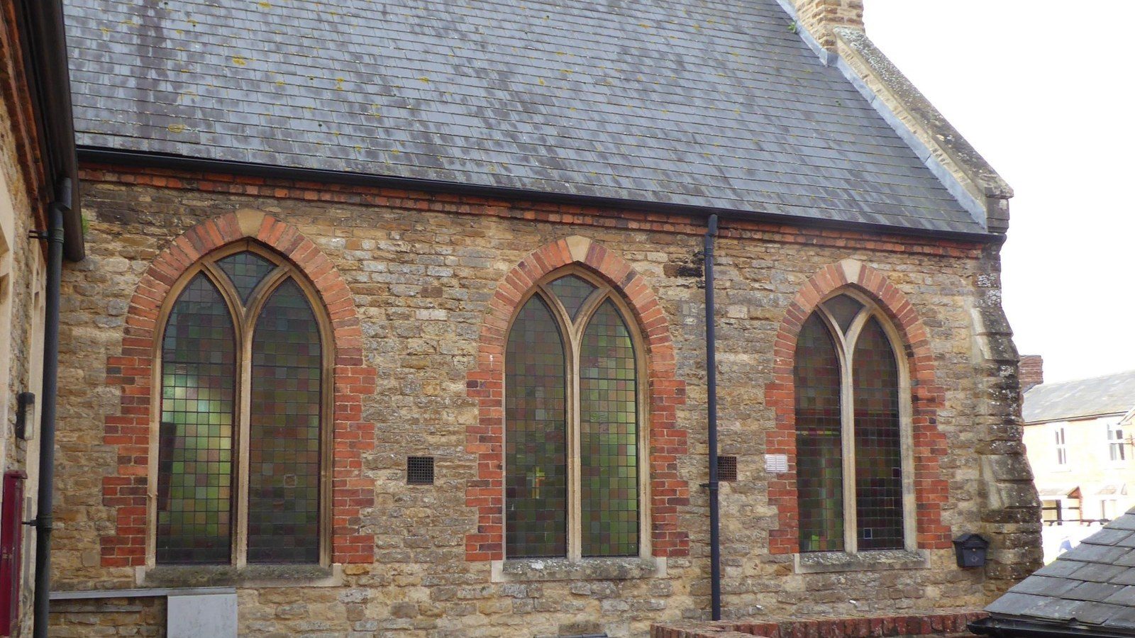 Side elevation of Towcester Methodist Church, an ironstone chapel with red brick arched stained glass windows
