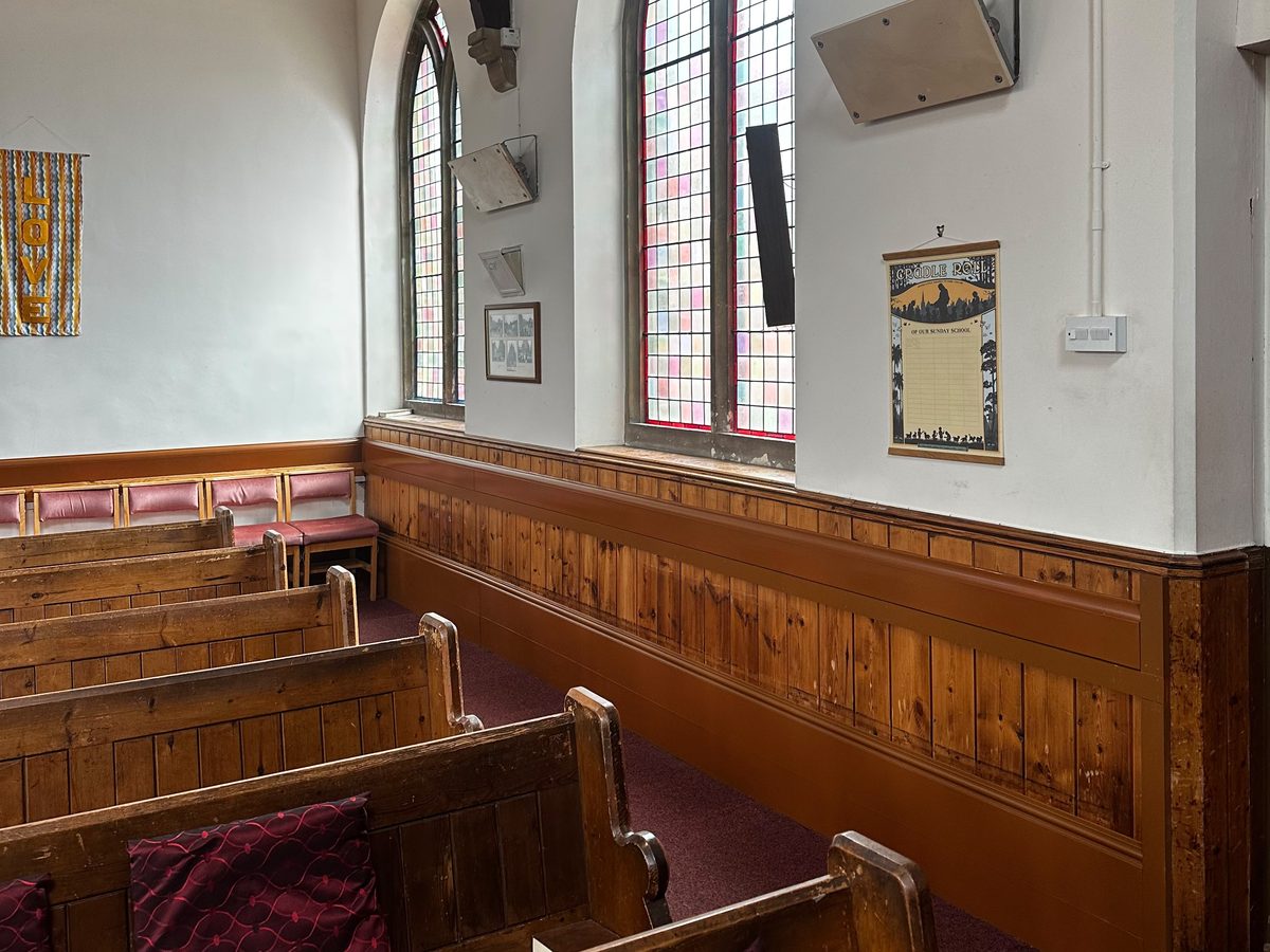 Finished church nave with wooden pews, stained glass windows and colour matched heating along the pine panelling