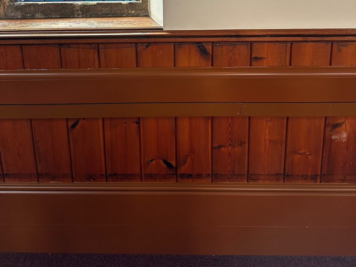 Close-up of ThermaSkirt-e skirting and mid-panel heating profiles colour matched to pine church panelling