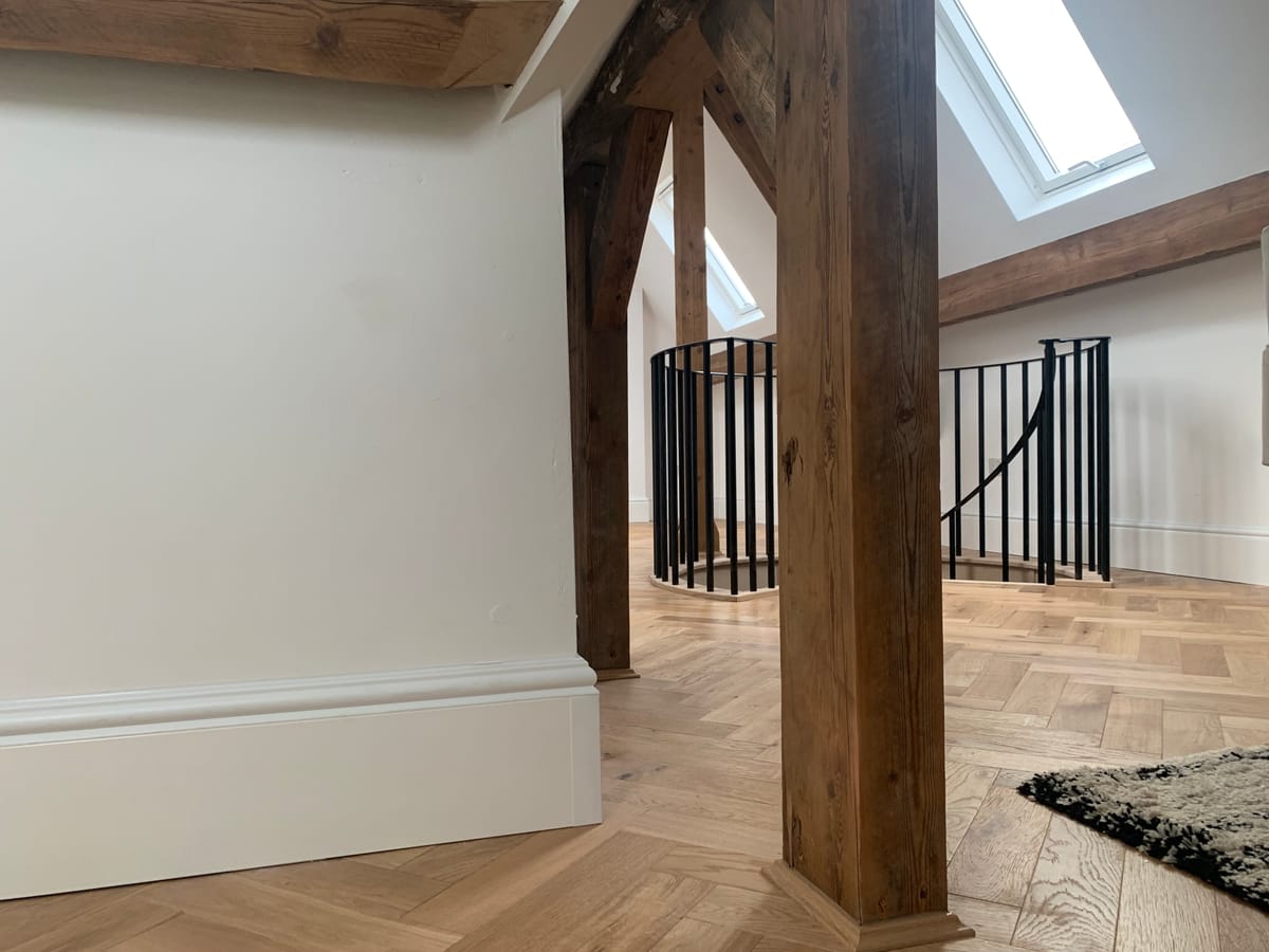 Loft conversion with exposed beam, herringbone parquet flooring, and ThermaSkirt Deco BM3 heating the upper floor space