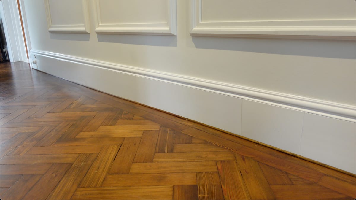 Period property hallway with ThermaSkirt Deco BM3 ogee profile running below panelled walls and herringbone parquet flooring