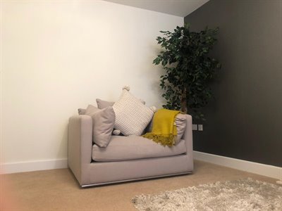 Compact grey sofa with cushions and yellow throw in a living room corner, ThermaSkirt skirting along the wall